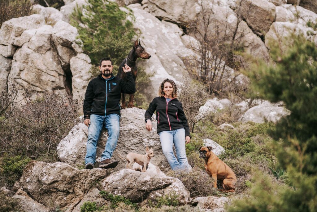 A couple enjoying a nature hike with their three dogs on rocky terrain.